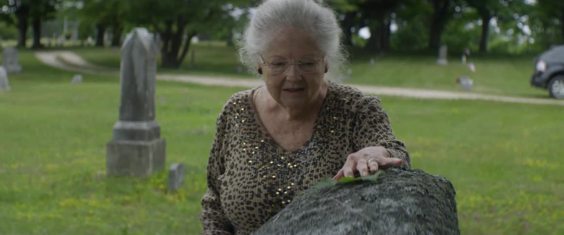 A woman puts a leaf on a headstone in a cemetery