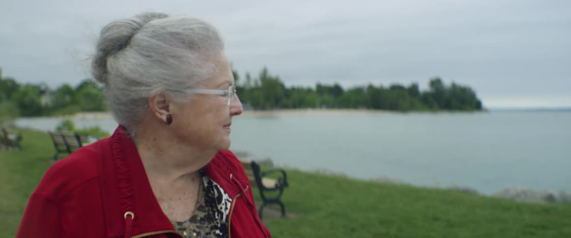 A woman looks out at the water as the wind blows her hair and jacket