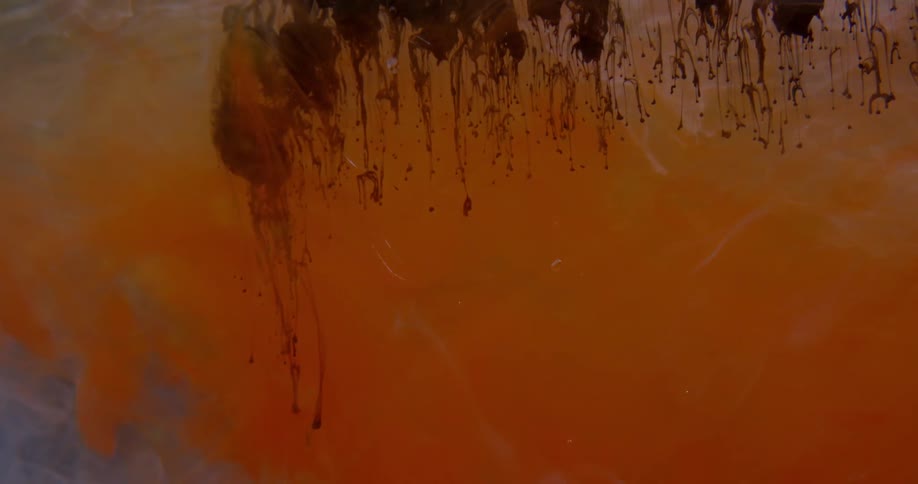 Brown dye drips down into clouds of orange dye in water