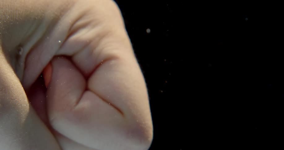 A woman is clenching her fist underwater in daylight