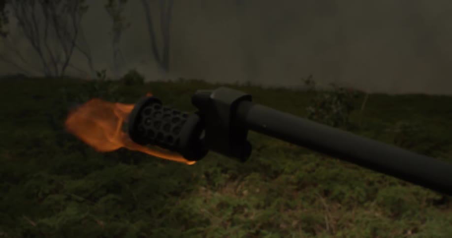 A flame thrower is pointed at a green field