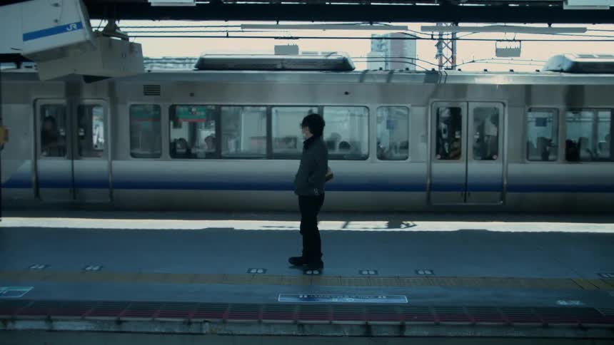A person is watching as a train leaves a commuter station in daylight