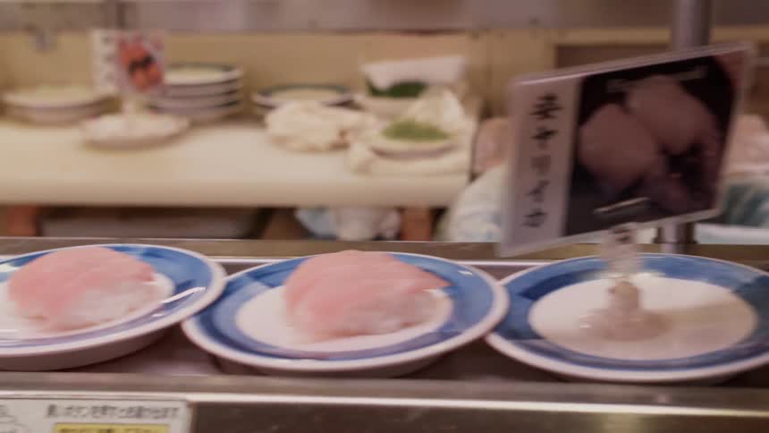 Plates with food on them go down a conveyor belt in a commercial kitchen as a chef walks by