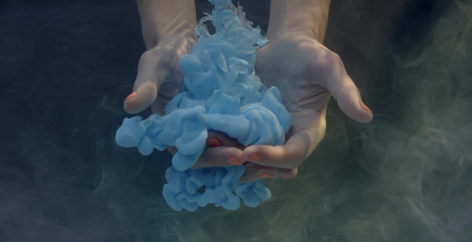 A cloud of blue dye floats down into cupped submerged hands