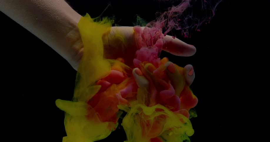 Colored dye is billowing and falling over a hand held underwater