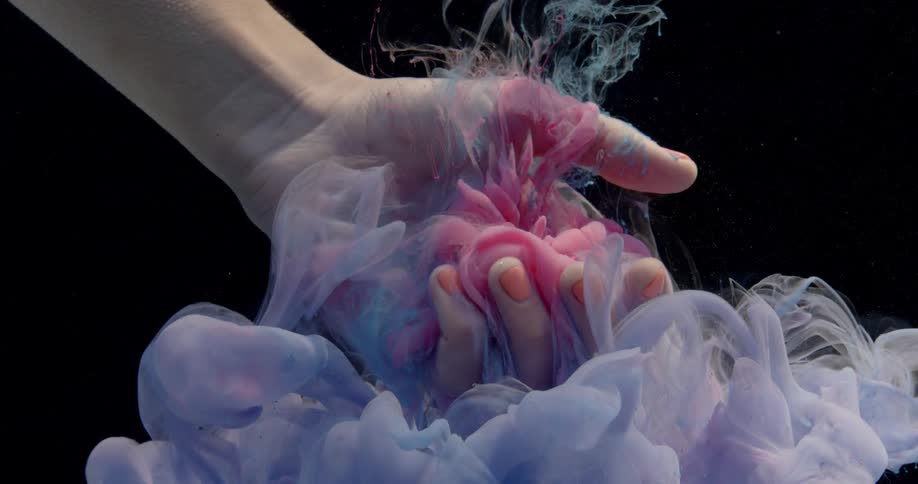 Clouds of dye fall and float around a woman's submerged hand