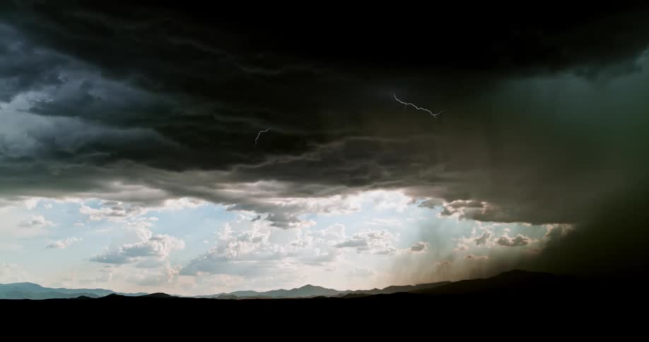 Lightning flashes and strikes the ground as a storm moves across a desert landscape