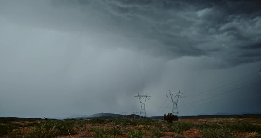 Lightning is flashing amid storm clouds as they move across a landscape in daylight