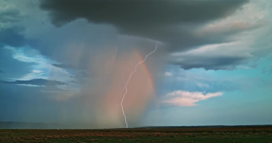 A rainbow begins to form as rain and lightning flashes