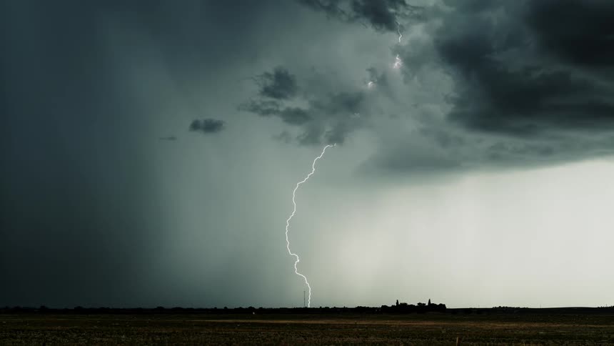 Lightning flashes and strikes the ground as a storm moves across a desert landscape
