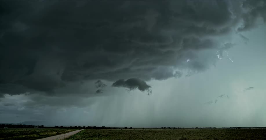 Lightning is flashing amid storm clouds as they move across a landscape at dusk