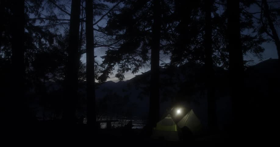 A light is shining in a tent on a lakeside at dusk