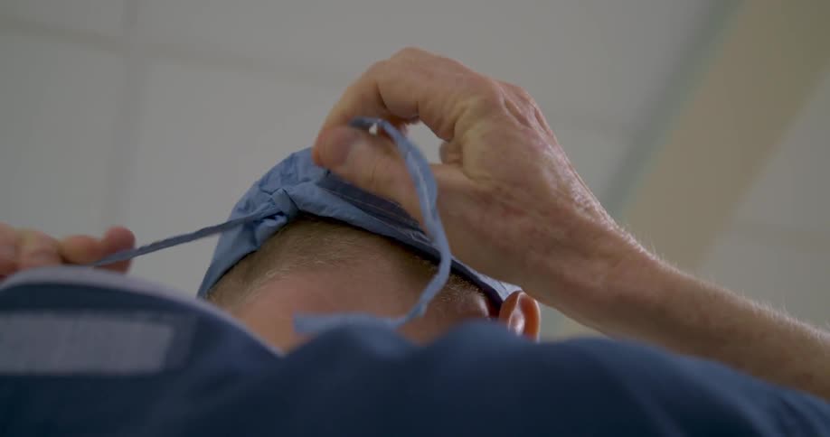 A surgeon is tying a cap on his head inside an operating room