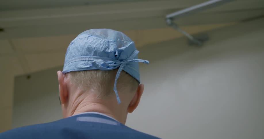 A surgeon is walking out of a doorway into a hall