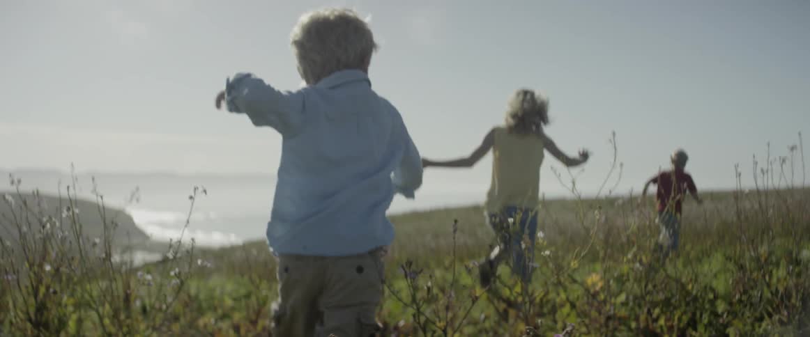 Children are running in a field on a coastal mountainside during the day