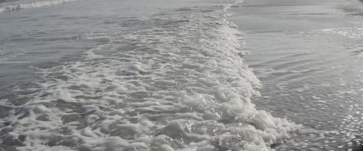 The waves move giving off bubbles on the shore