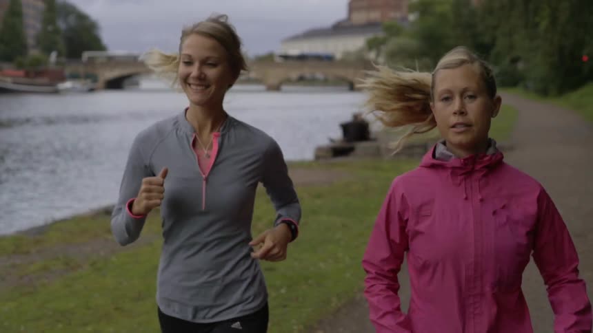 Female friends wear colorful windbreakers while running along a dirt trail in summer.