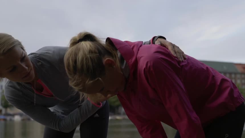 A woman checks on another who is bent over catching her breath