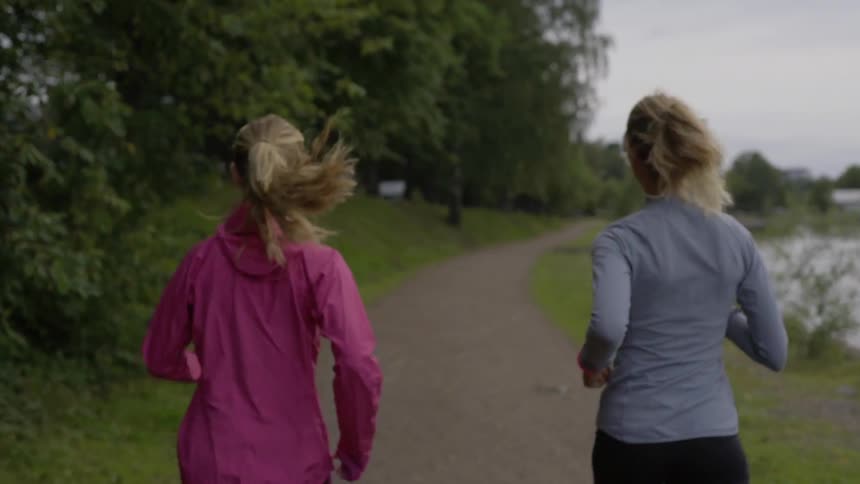 Two female runners practice their daily cardio fitness routine near a calm river.
