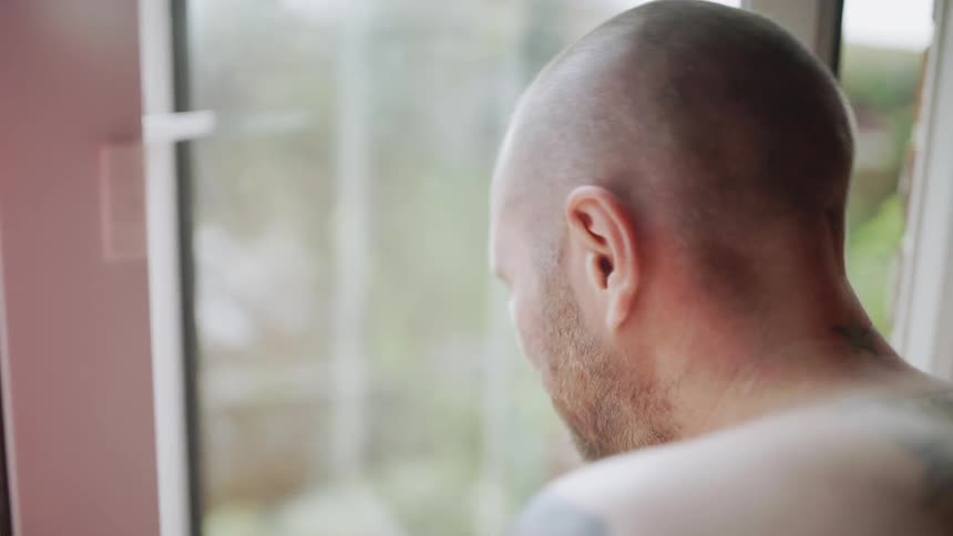 A man looking out an open window backs up and turns away
