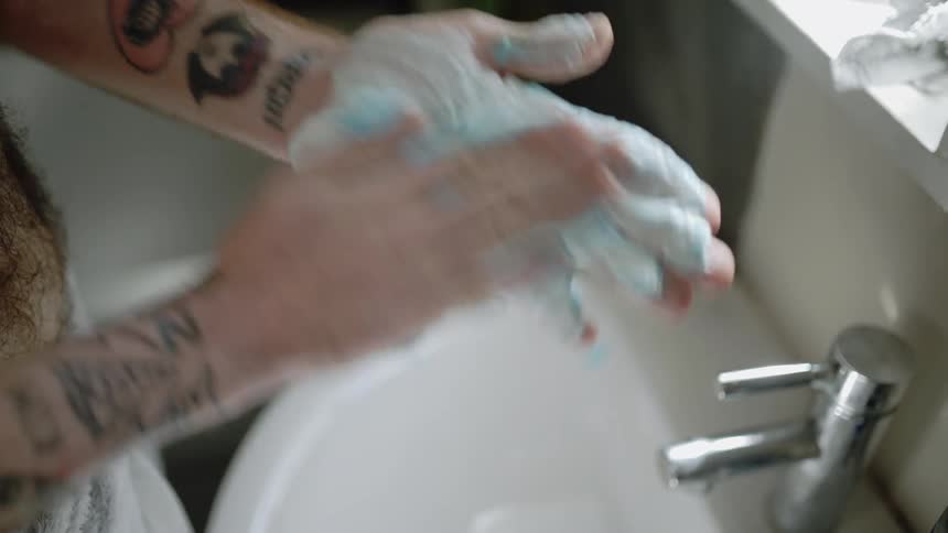 Man stands over sink and mixes shaving cream in his hands