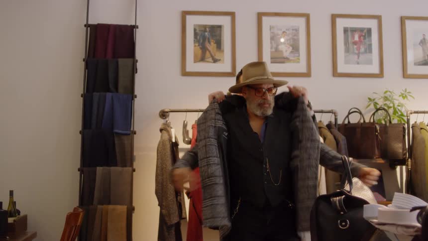 A man in a suit shop helps a customer try on a jacket