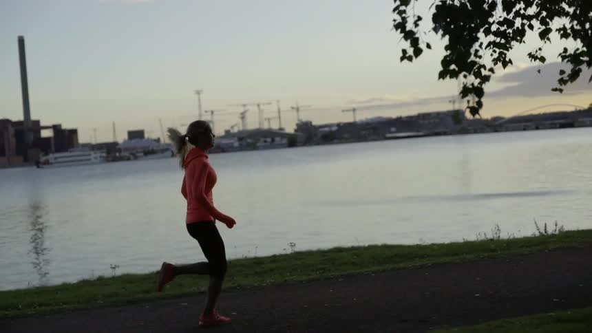 A sporty woman practices cardio training outdoors on a path during twilight hours.