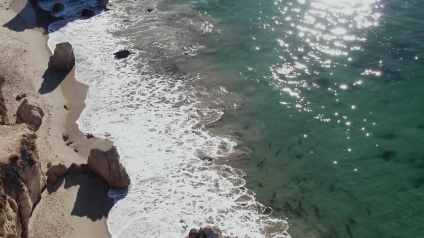 Ocean waves splash onto the shore on a sunny day