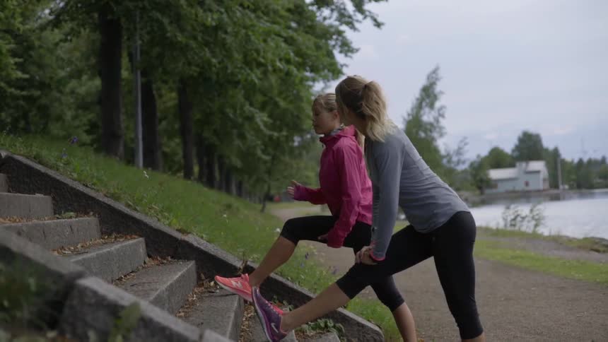 Two athletic women stretch their legs on stone stairs before an outdoor run.