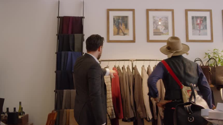 Two men greet each other and hug and look at clothing together