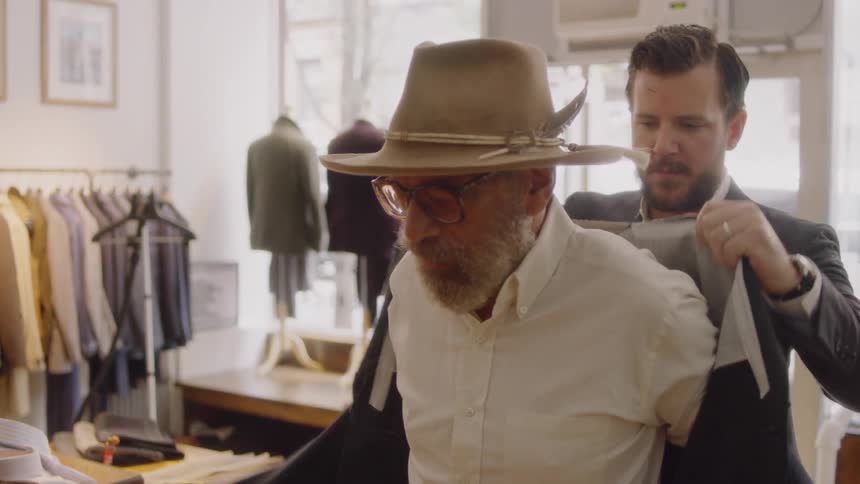A man tries on a jacket with assistance from the shop owner