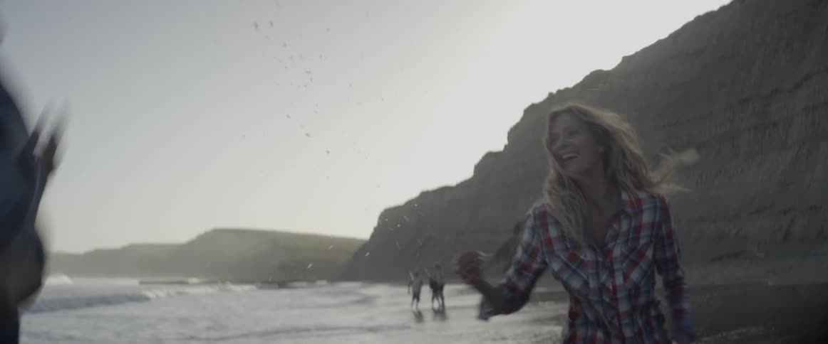 A man and woman run on the beach as children play by the water
