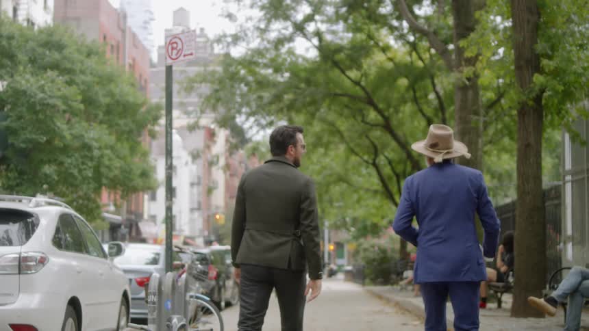 Two people walk down the sidewalk together talking