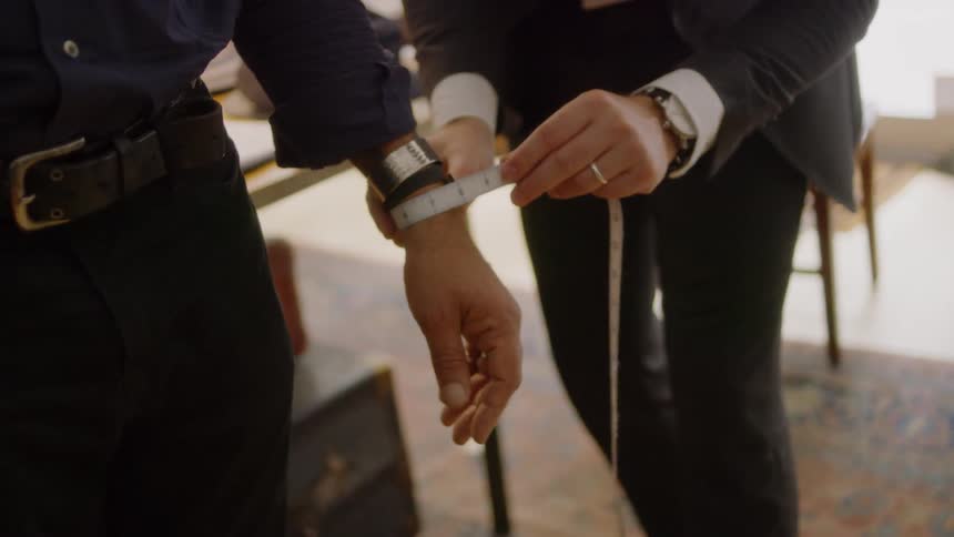 Tailor measures the wrist of a man with a measuring tape