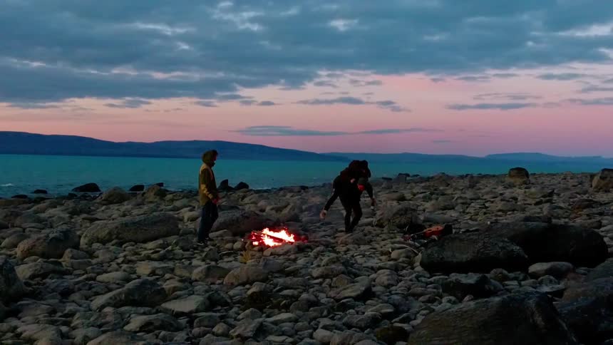 Three people play near a bonfire on the beach