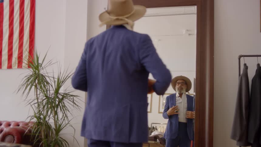 Man puts on his suit jacket and looks in a mirror