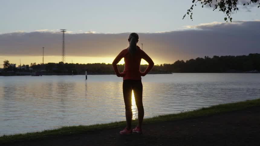An athletic female runner rests by the water during a peaceful evening workout.