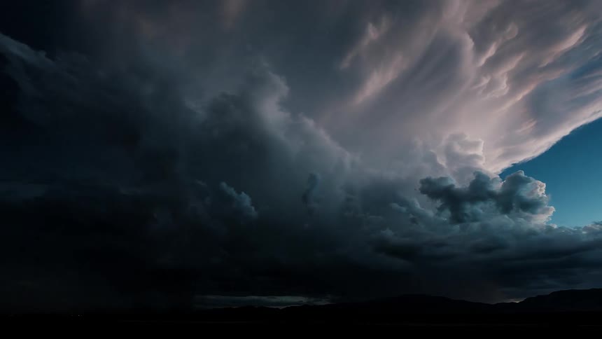 Many white and dark clouds over mountains with lightning flashing