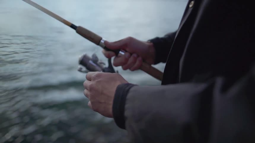 A man holding a fishing pole and reeling the line in over the water