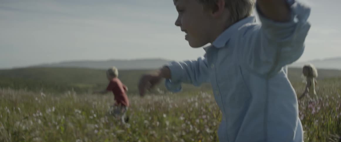 Three children are running through a mountain field in daylight