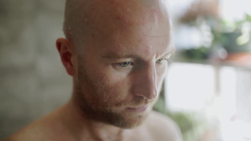 A bald man stands indoors