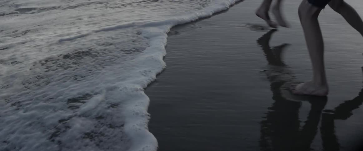 Two people walk barefoot on a beach