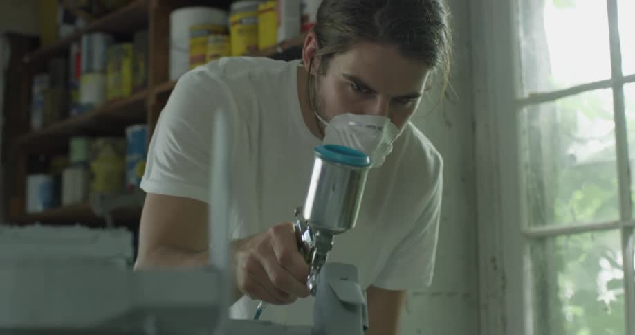 A man wears a face mask while using a paint sprayer
