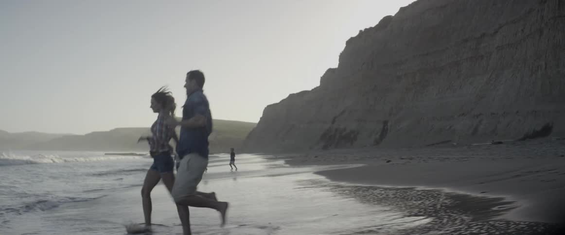 Man and woman run on the beach through the sand and water