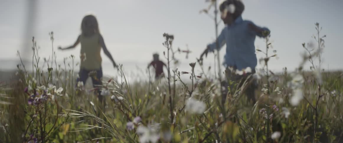 Two boys and a girl running through high grass and plants on a cloudy day