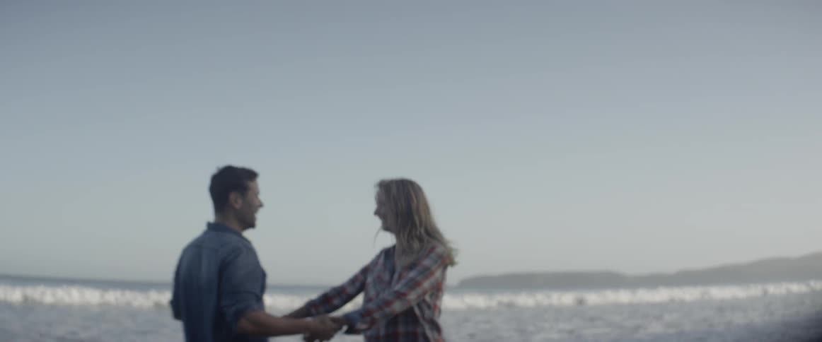Man and woman hold hands as they play on the beach