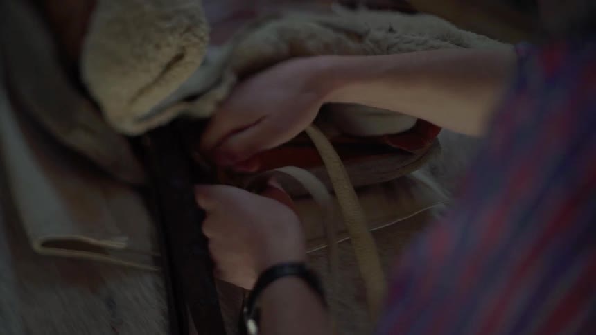A person attaches a saddle to a horse