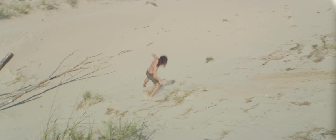 A man jumps off a hill and lands on a sandy slope