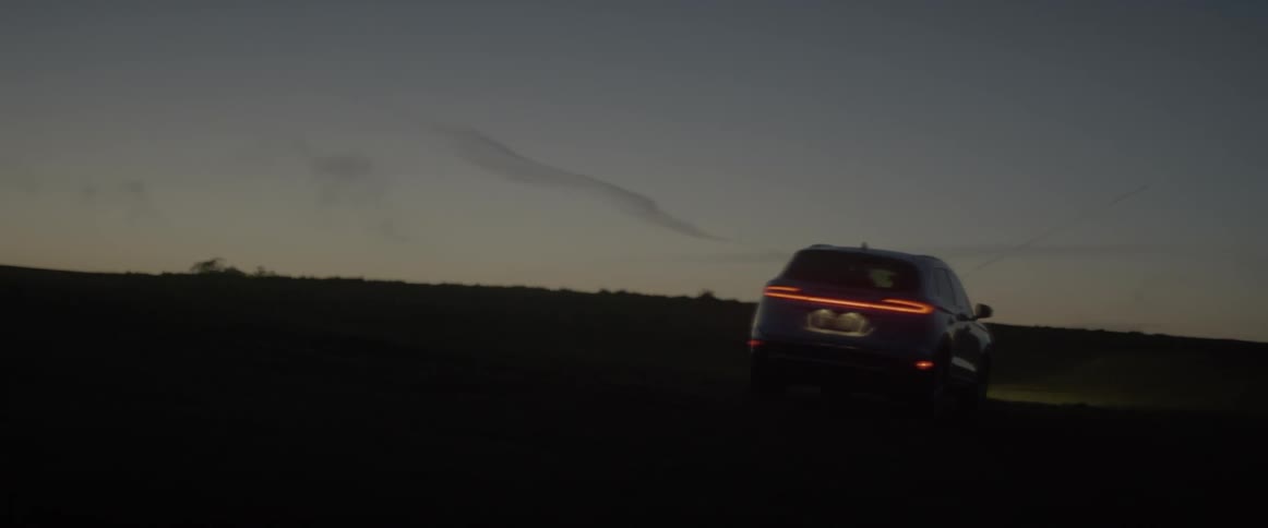 A car drives across a rural field at dusk