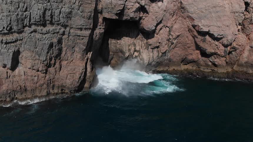 Waves are crashing against cliffs in daylight
